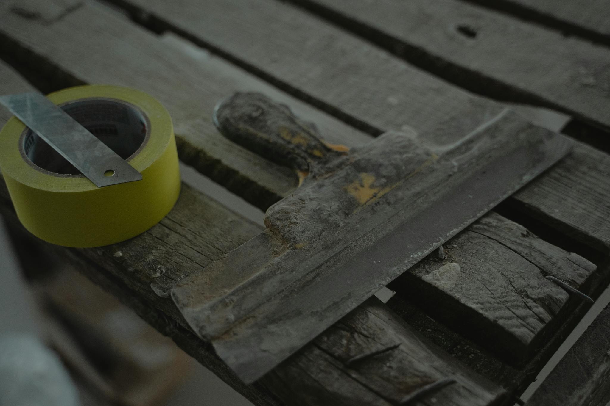 Close-up of a spatula and duct tape on an aged wooden surface. Perfect for DIY and renovation themes.